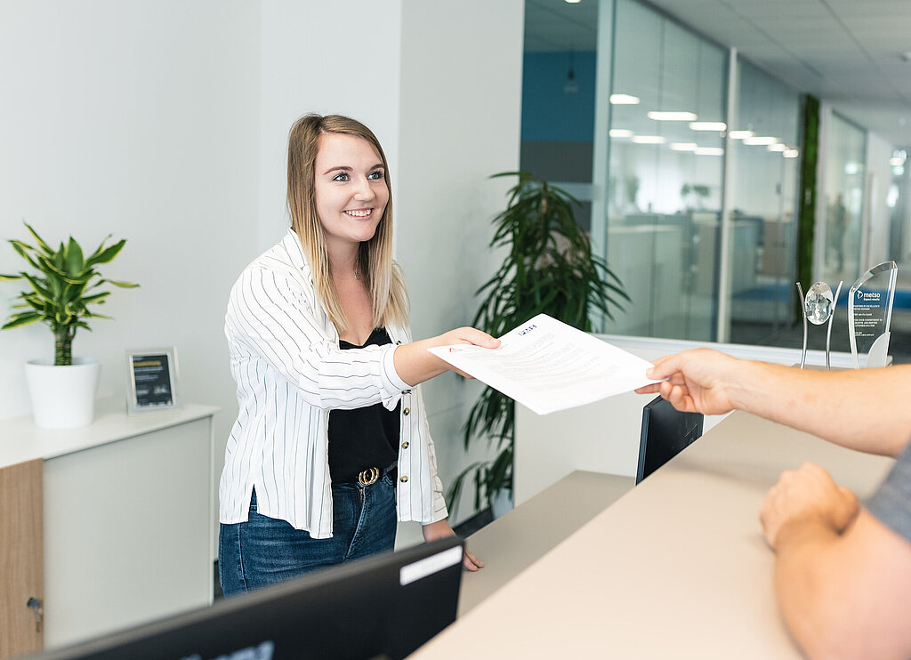 Mitarbeiterin überreicht Mitarbeiter Unterlagen am Empfang.