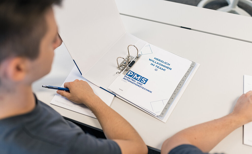 Mitarbeiter sitzt am Tisch mit geöffneter Mappe vor sich.