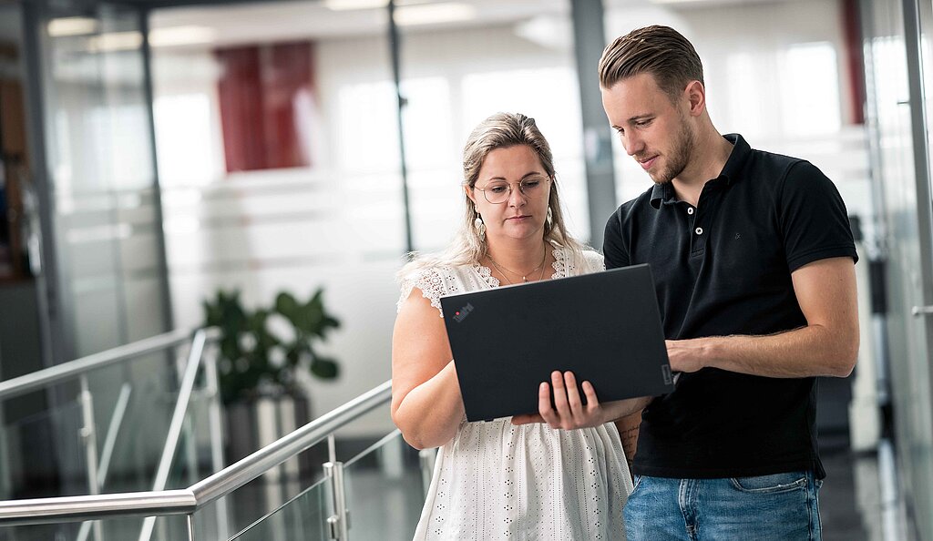 Mitarbeiter der PSI Powerful Solutions beugen sich am Gang über einen Laptop
