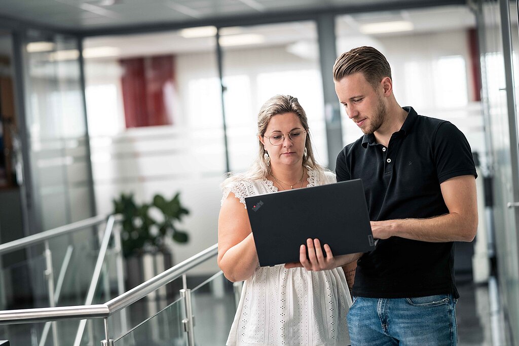 Mitarbeiter der PSI Powerful Solutions beugen sich am Gang über einen Laptop