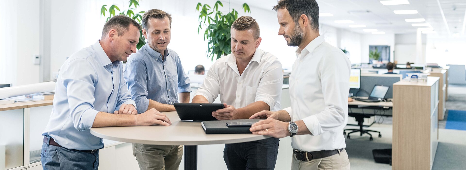Vier Männer im Meeting am Stehtisch im Großraumbüro der PMS