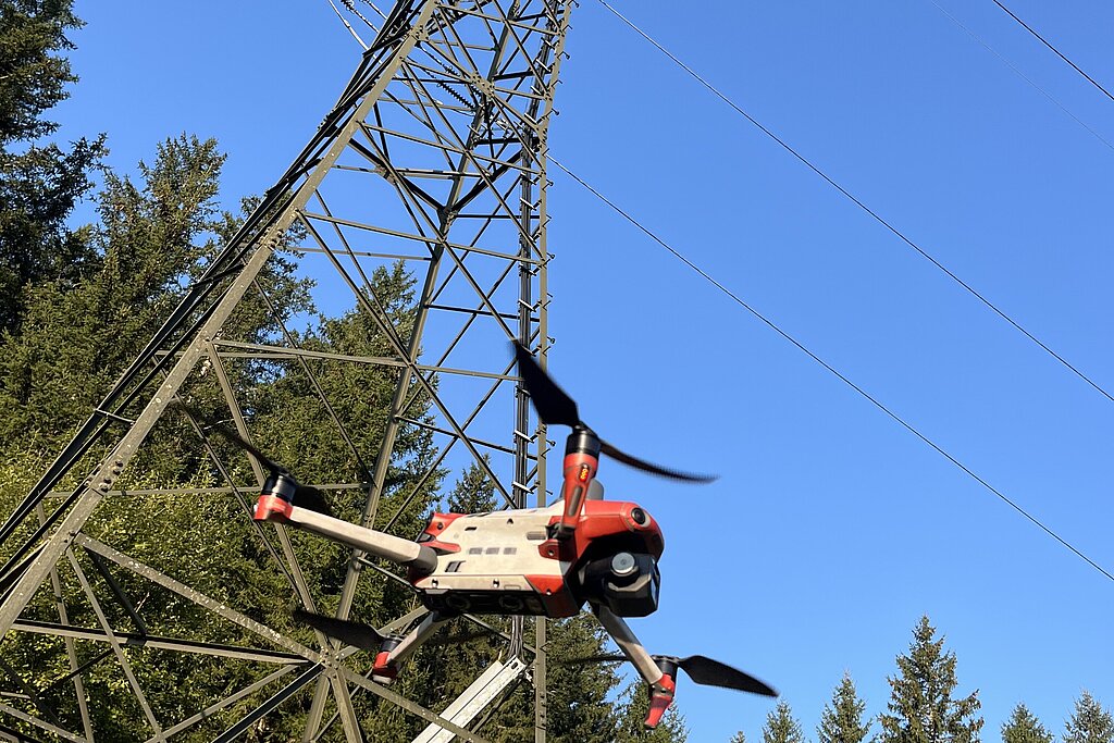 Eine Drohne in der Luft, im Hintergrund ein großer Strommast 