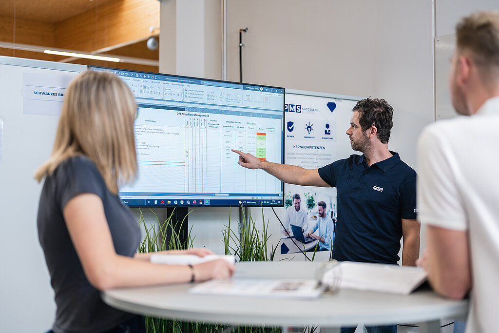 Drei Mitarbeiter in einer Besprechung deuten auf einen Bildschirm