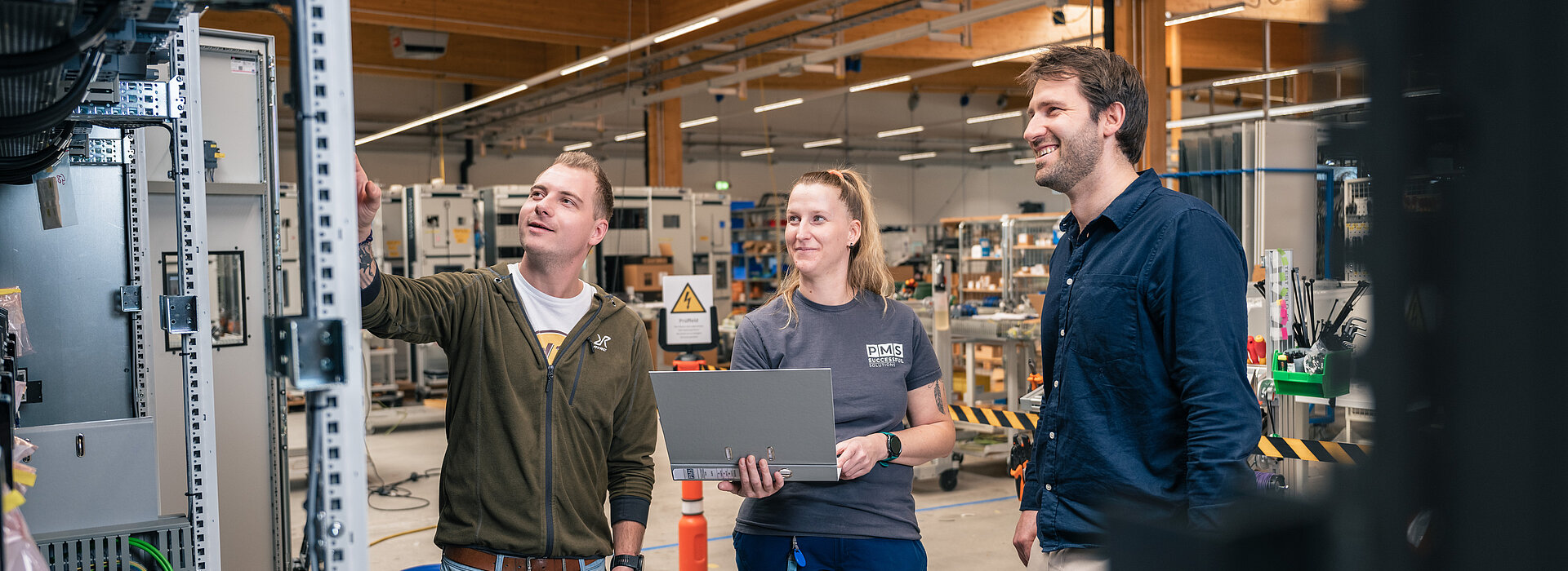 Fertigungsmitarbeiter:innen mit dem Geschäftsführer beim Prüfen einer Schaltanlage in der modernen Fertigung