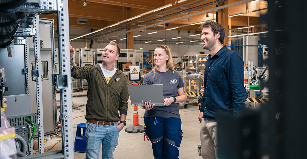 Fertigungsmitarbeiter:innen mit dem Geschäftsführer beim Prüfen einer Schaltanlage in der modernen Fertigung