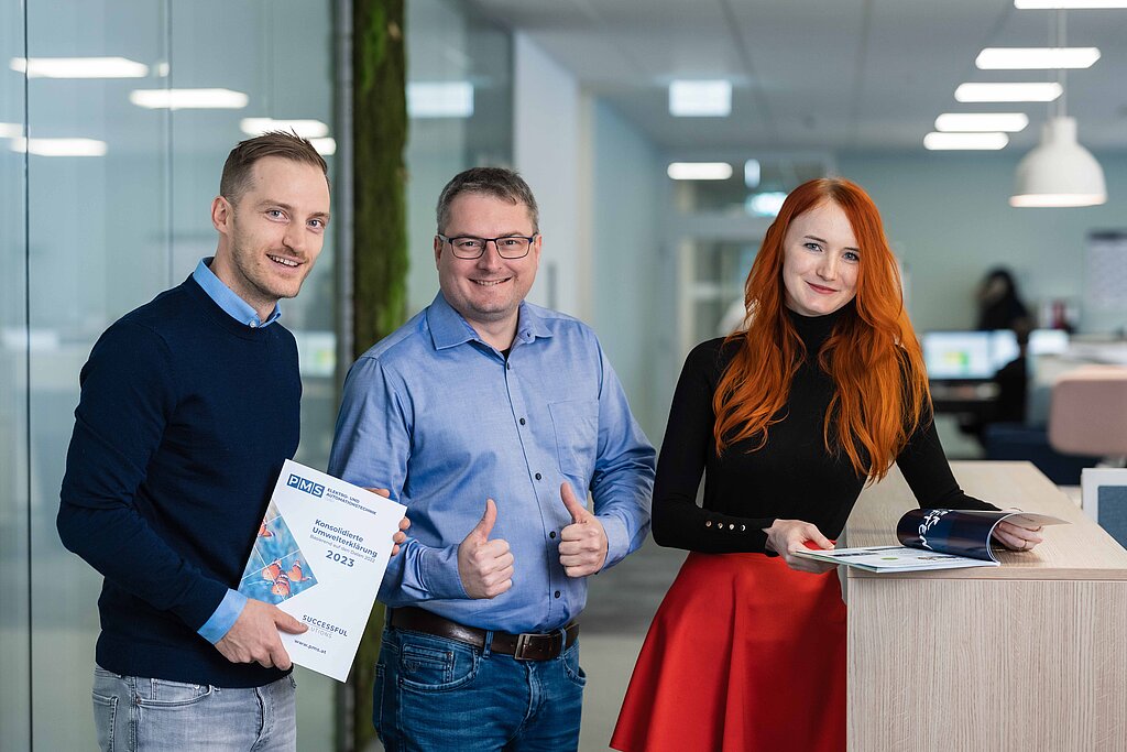 Zwei Männer und eine Frau präsentieren die neue Umweltbroschüre, dahinter ein Großraumbüro