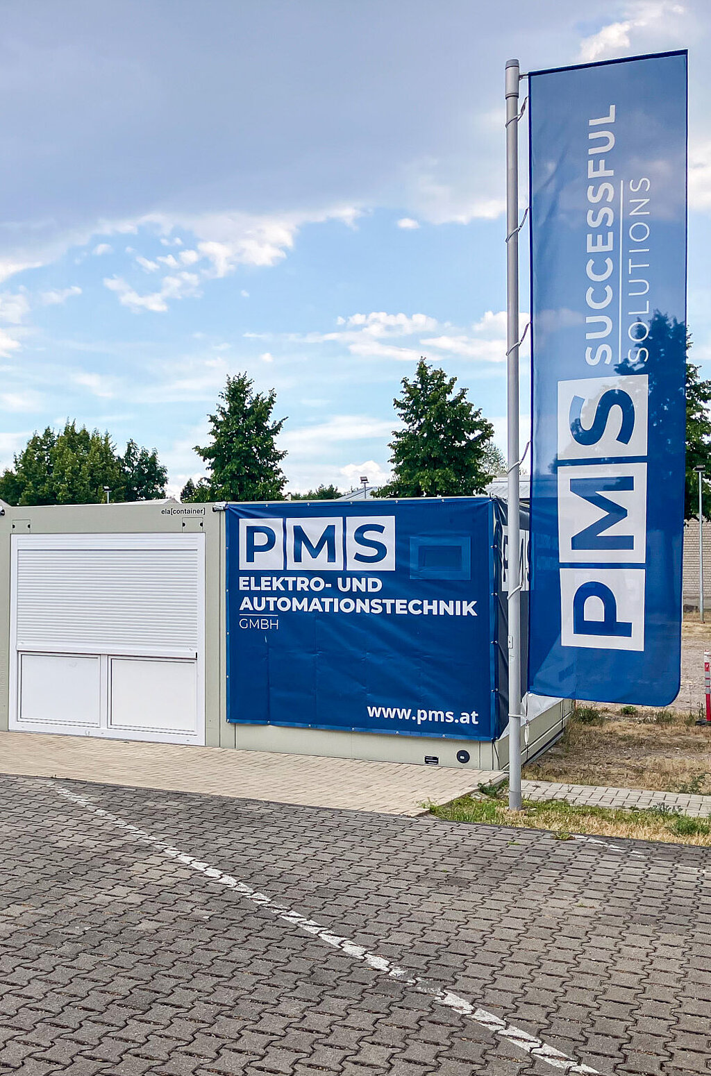 PMS Elektro- und Automationstechnik GmbH mit Fahne und Container vor Bäumen