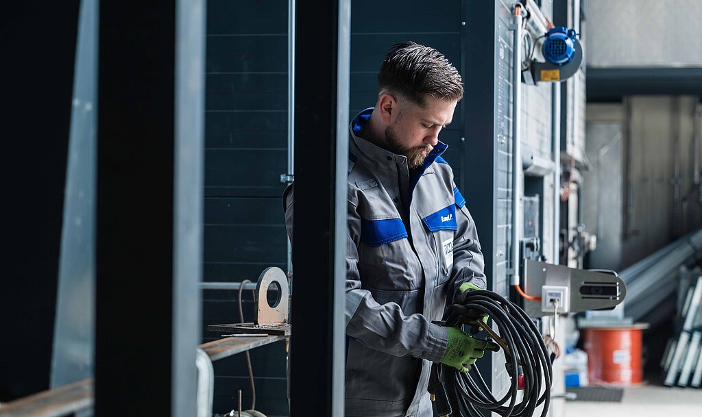 Ein Mitarbeiter der PMS Alternative Energie Systeme mit einer Kabelrolle in einem Heizkraftwerk