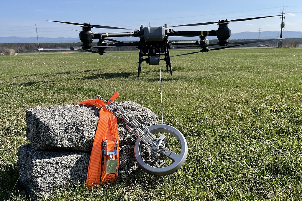 Eine Drohne bestückt mit 2 Pflastersteinen, zusammengehalten von einem orangen Gurt, vor dem Start