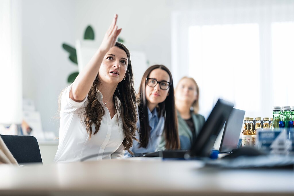 Mitarbeiterinnen in einem Besprechungsraum, eine deutet mit der Hand, vor ihr der geöffnete Laptop