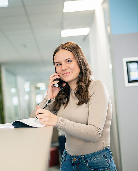 Ein Bürokauffraulehrling macht sich beim Telefonieren Notizen am Empfang im  PMS Office