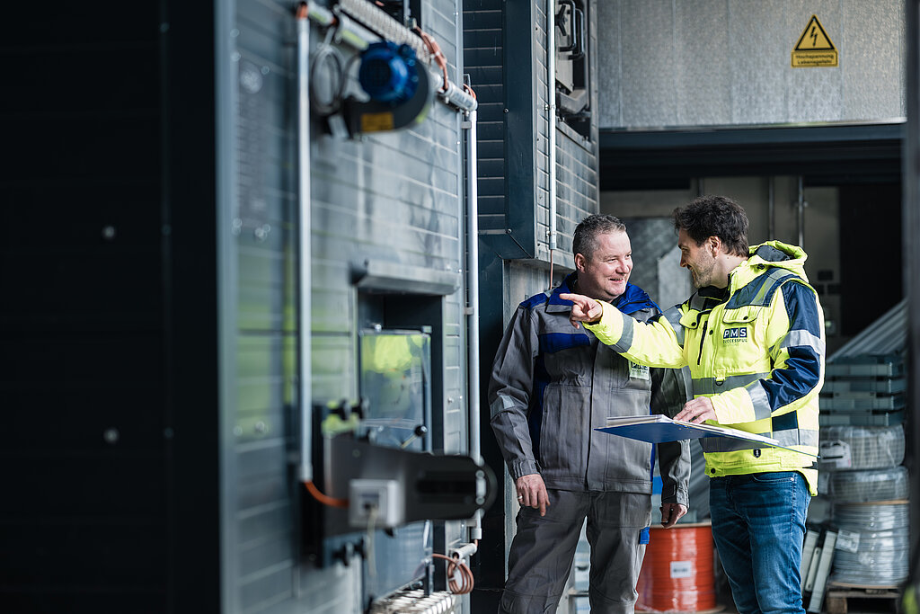 ein Servicemitarbeiter und ein Projektleiter der PMS mit einer Mappe in der Hand, im Gespräch in einem Heizwerk