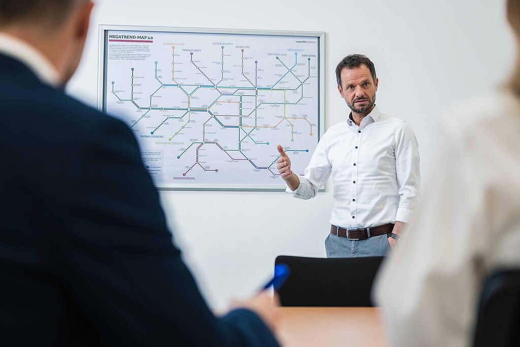 der Geschäftsführer des PMS Technikums erläutert seinen Gesprächspartnern einen Projektplan