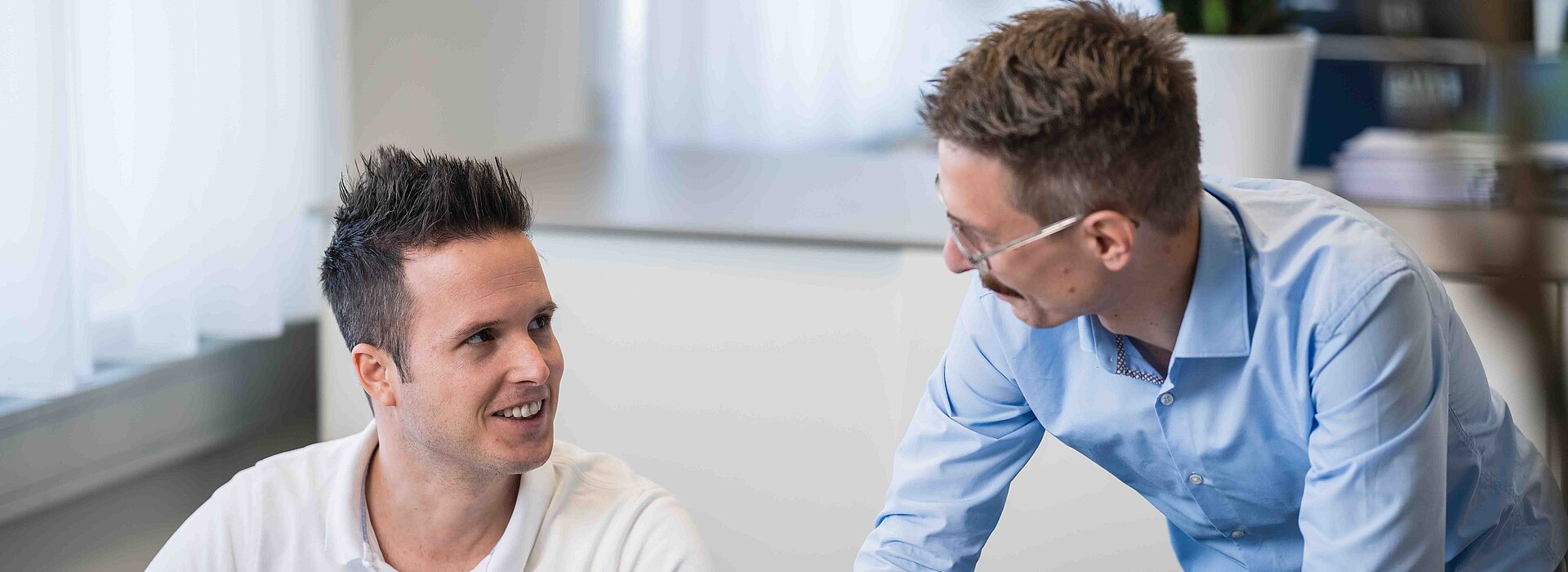 zwei Engineeringmitarbeiter im Gespräch vor dem großen Bildschirm am Arbeitsplatz im Büro