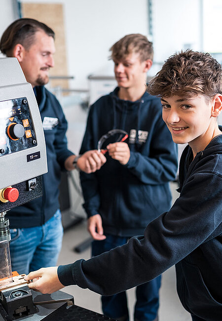 Ein Lehrlingsausbilder insturiert 2 Lehrlinge, einer hantiert an einer Maschine